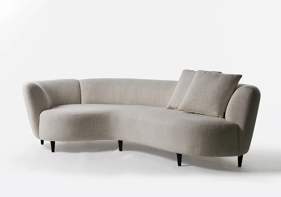 sofá curvo claro com duas almofadas em primeiro plano e cinco pés escuros em um fundo branco.