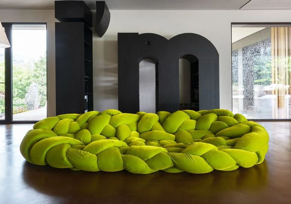 Sofá de design moderno com estrutura tubular preenchida com várias densidades de espuma na cor verde claro, visto de frente, em uma sala de piso de porcelato e janelas de vidro.