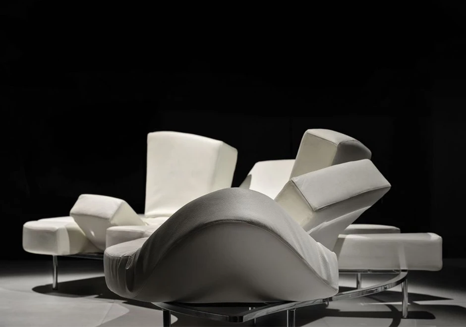 Sofá de design futurista, com estrutura de aço e mecanismo flexível com diferentes inclinações, na cor branca, visto de lado em um fundo preto.