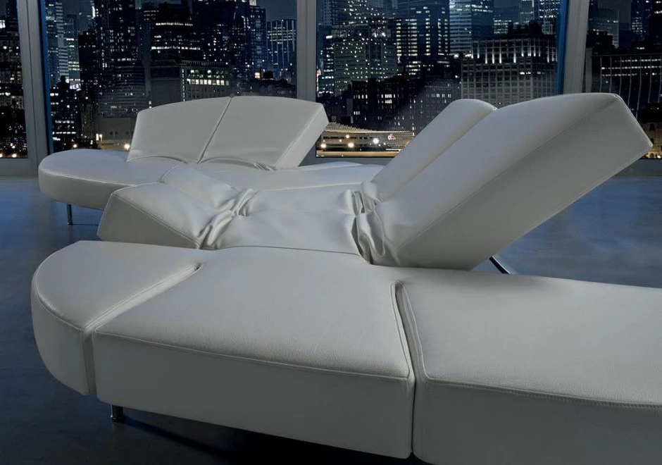 Sofá de design futurista, com estrutura de aço e mecanismo flexível com diferentes inclinações, na cor branca, visto de lado em uma sala com parede de vidro.