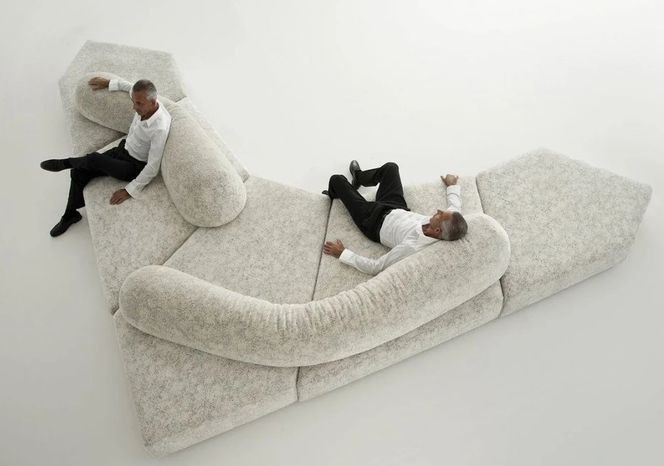 Sofá de design moderno, com pés em ABS, revestido em espuma e com estofado em tecido cinza, visto de cima, com dois homens sentados, em um fundo branco.