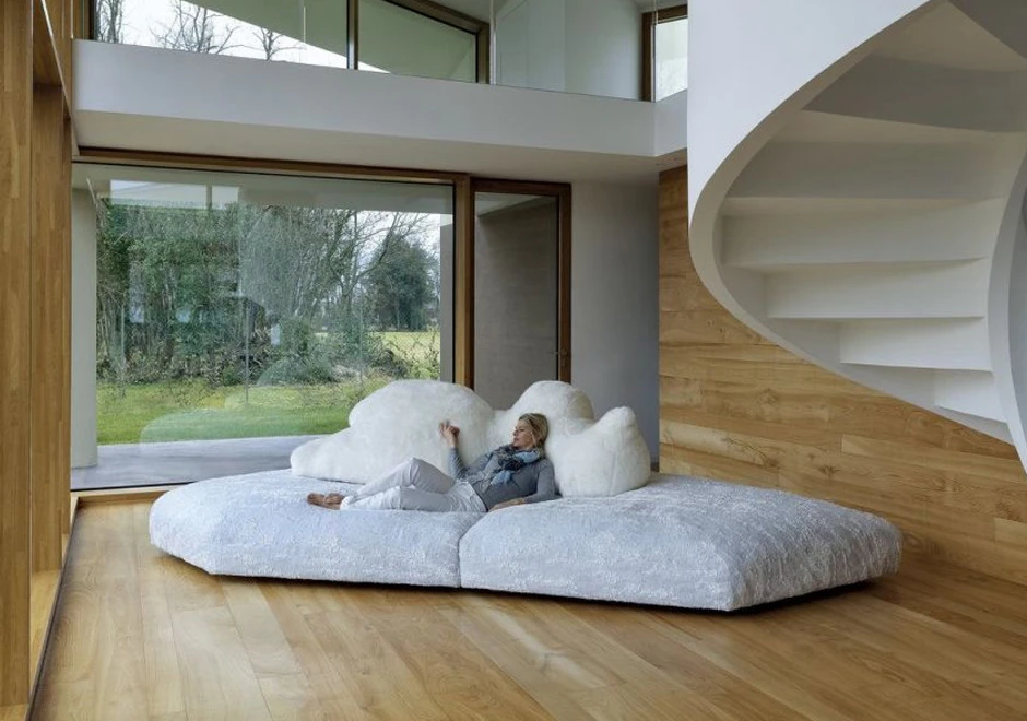 Sofá de design com estrutura de madeira, estofado em plumas e tecido na cor branco, visto de frente, com uma pessoa deitada, em uma sala clássica.