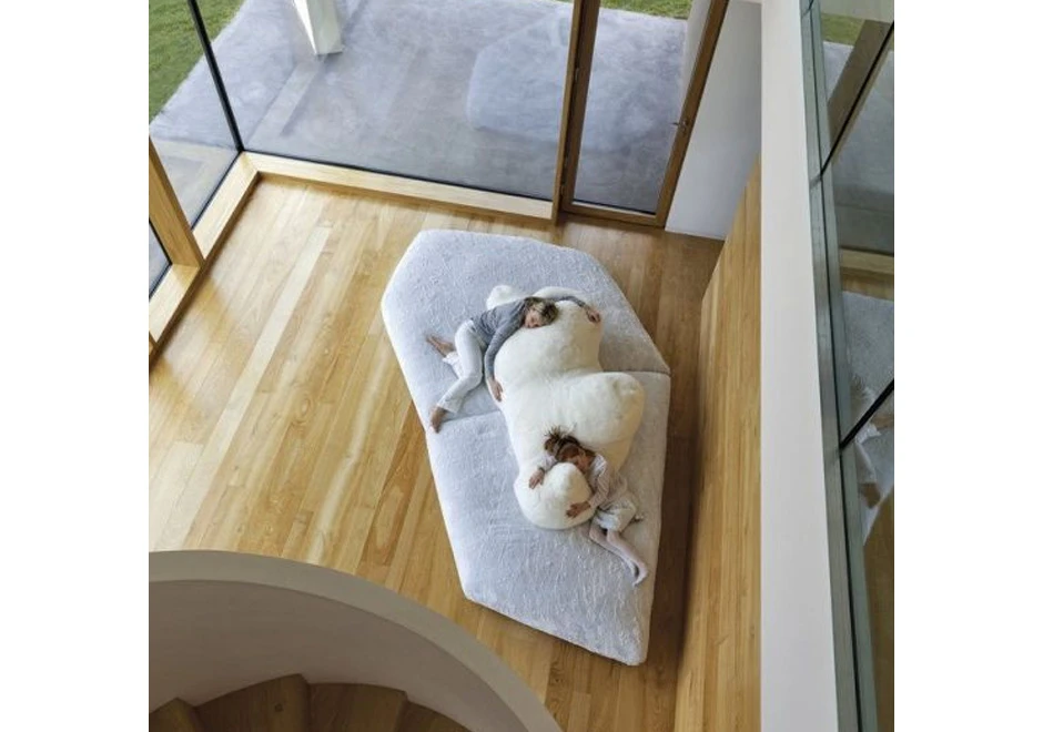 Sofá de design com estrutura de madeira, estofado em plumas e tecido na cor branco, visto de cima, com duas pessoas deitadas, em uma sala clássica.