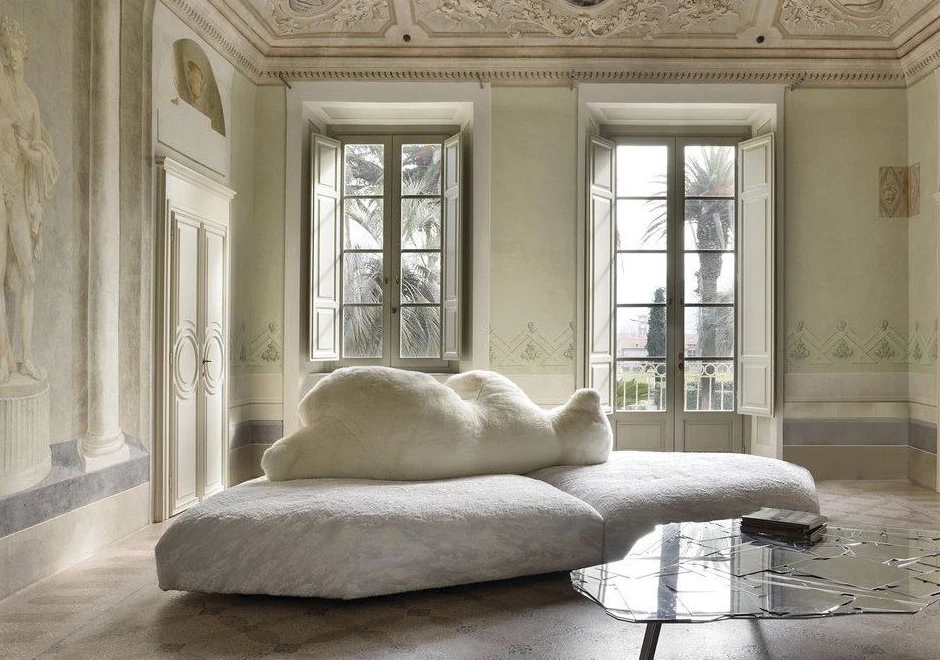 Sofá de design com estrutura de madeira, estofado em plumas e tecido na cor branco, visto de lado, em uma sala clássica.