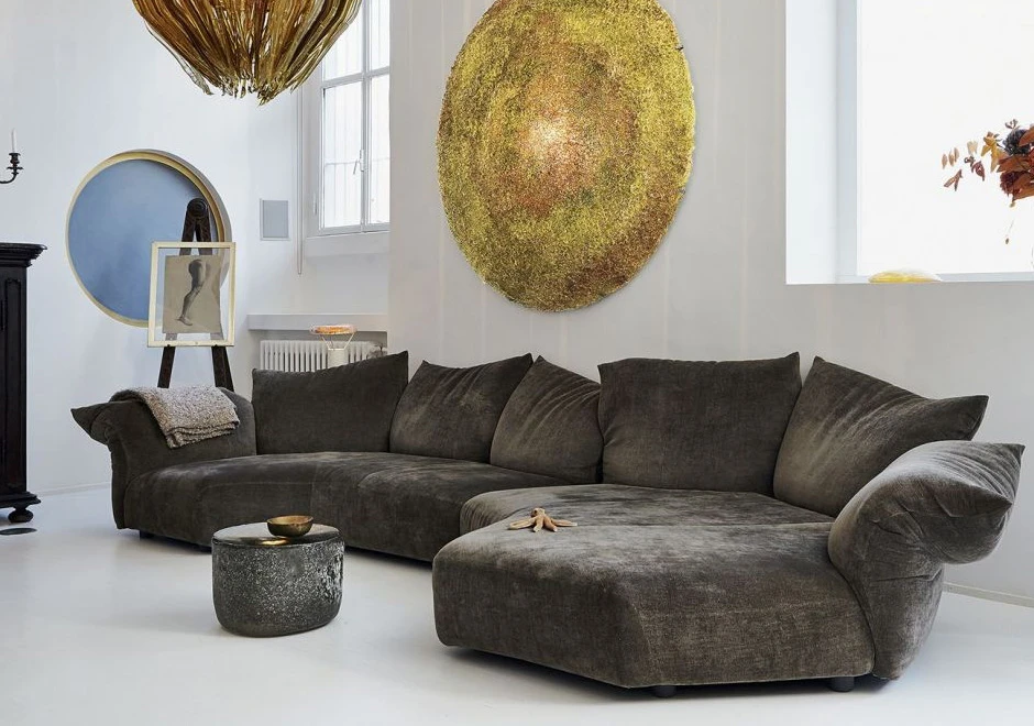 Sofá de design, com estrutura metálica, almofadas e braços reclináveis,cinza escuro, visto de lado em uma sala moderna.