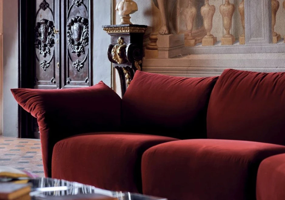 Sofá de design, com estrutura metálica, almofadas e braços reclináveis, vermelho, visto de frente em uma sala estilo clássico.