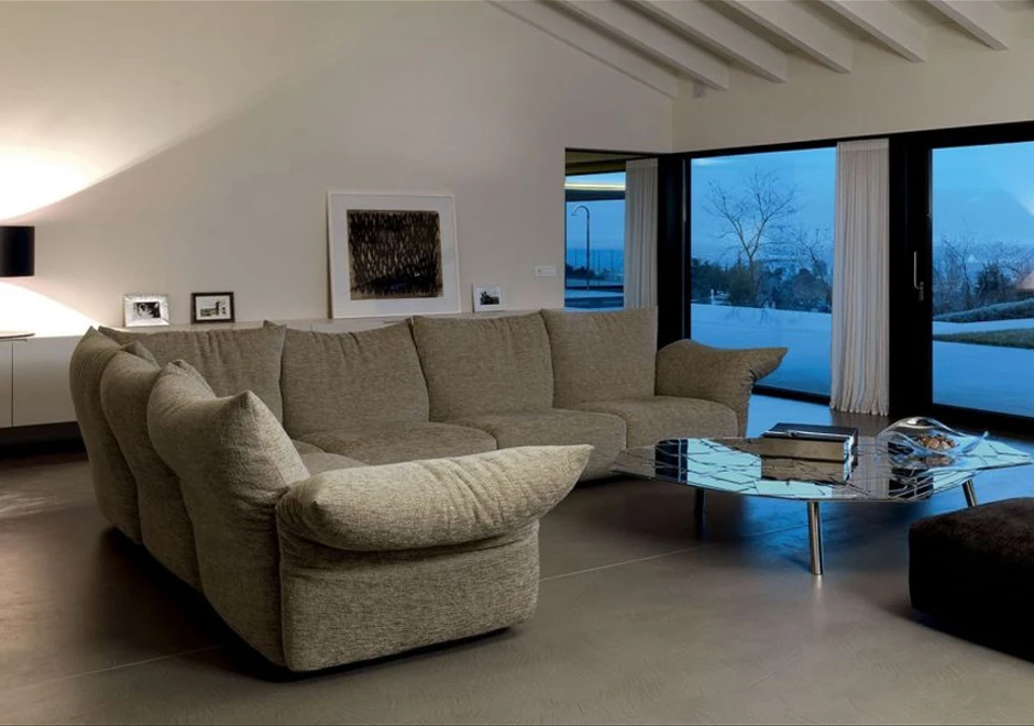 Sofá de design, com estrutura metálica, almofadas e braços reclináveis,bege, visto de lado em uma sala moderna.