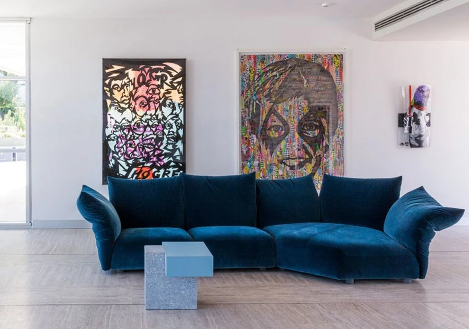 Sofá de design, com estrutura metálica, almofadas e braços reclináveis,azul, visto de frente em uma sala moderna.