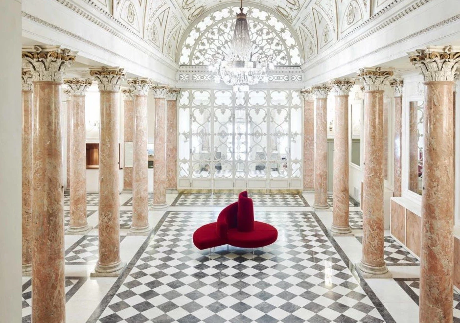 Sofá ilha,com pés em aço cromado e estofado de veludo vermelho, visto do alto em um salão clássico.