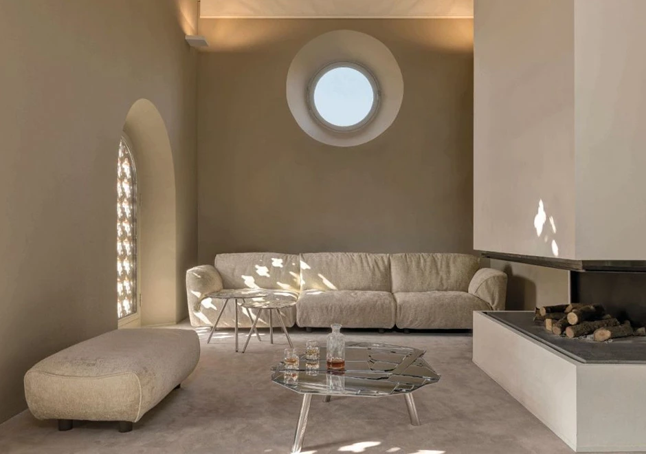 Sofá modular com encosto articulado e estofado em tecido creme, visto de frente, em uma sala aconchegante.