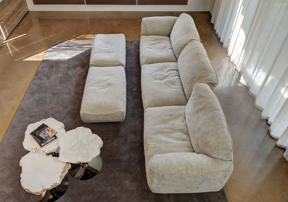 Sofá modular com encosto articulado e estofado em tecido creme, visto de cima, em uma sala aconchegante.