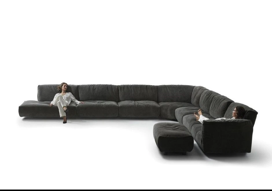 Sofá modular com encosto articulado e estofado em tecido preto, visto de frente, com duas mulheres sentadas nele, em um fundo branco.