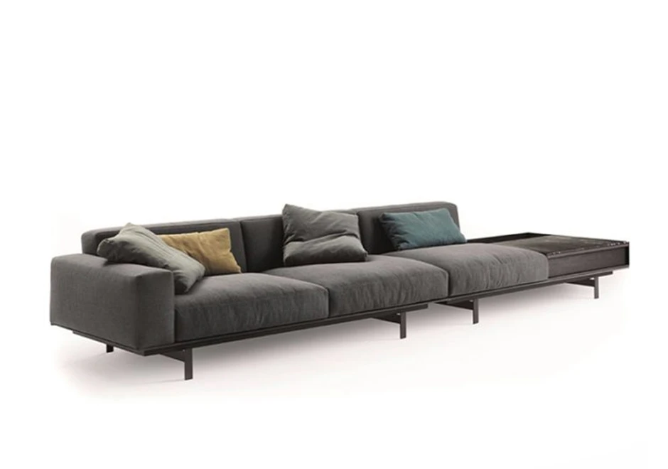 Sofá modular com estrutura de metal, estofado em tecido cinza e almofadas decorativas, visto de lado em um fundo branco.