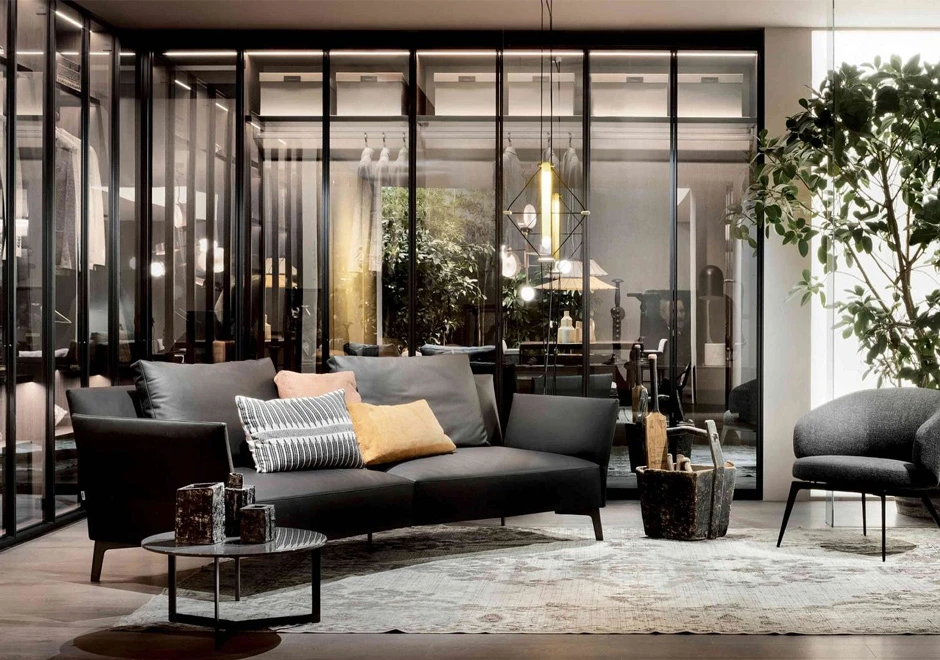 Sofá de design clássico, com estrutura de metal e estofado em couro cinza, visto de lado, em uma sala moderna.