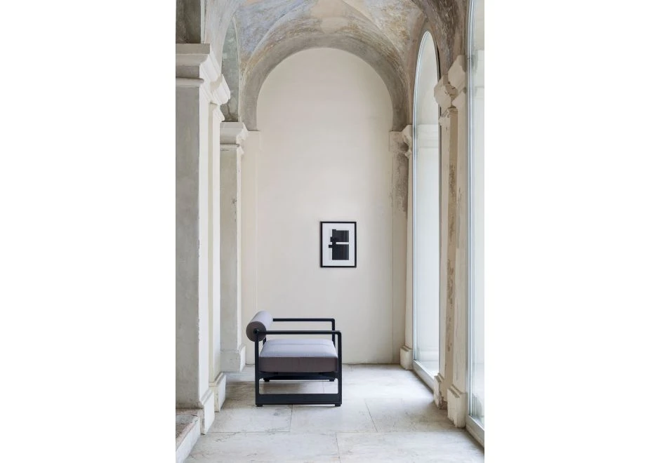 Sofá contemporâneo com estrutura em ferro fundido, e estofado em espuma, cinza, visto de lado em uma sala moderna de pilatras grandes.