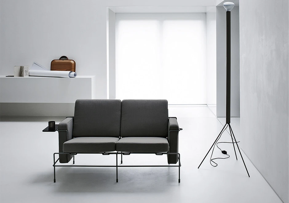 Sofá modular, com estrutura em aço e almofadas em espuma, em tecido cinza, visto de frente em uma sala de parede branca.