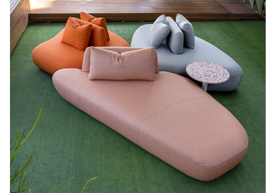 Sofá Pedras Outdoor com tecidos azul, rosa e laranja e almofadas decorativas, visto de frente em uma area externa.