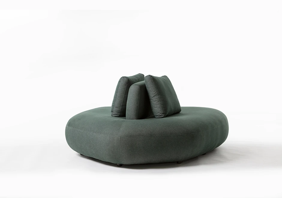 Um módulo de sofá Pedras modular, com estrutura de madeira, com almofadas decorativas, estofado em tecido verde, visto de lado, em um fundo branco.