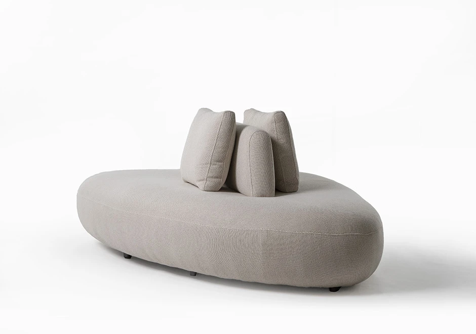 Um módulo de sofá Pedras modular, com estrutura de madeira, com duas almofadas decorativas, estofado em tecido cinza, visto de lado, em um fundo branco.