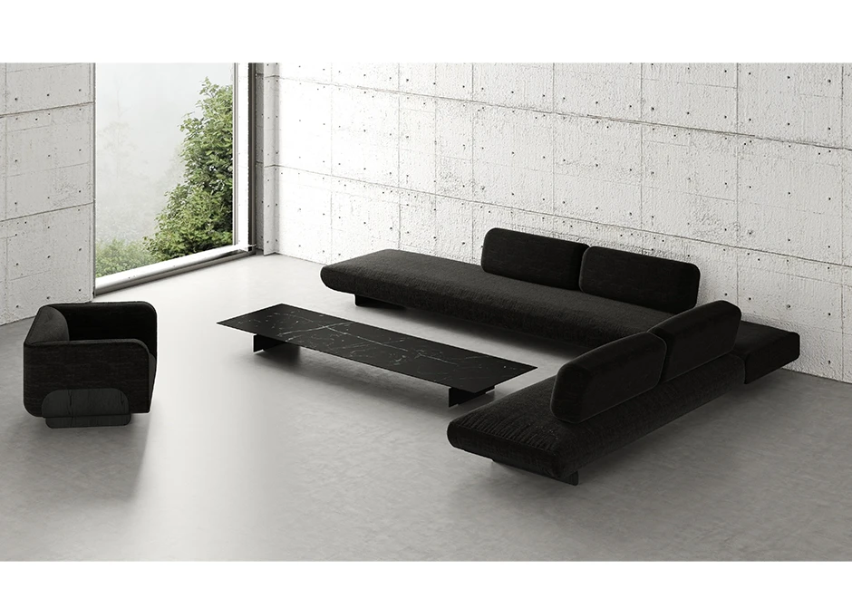 Sófa modular, com base de metal, revestido em espuma, estofado em tecido preto, visto de lado em uma sala com duas poltronas.