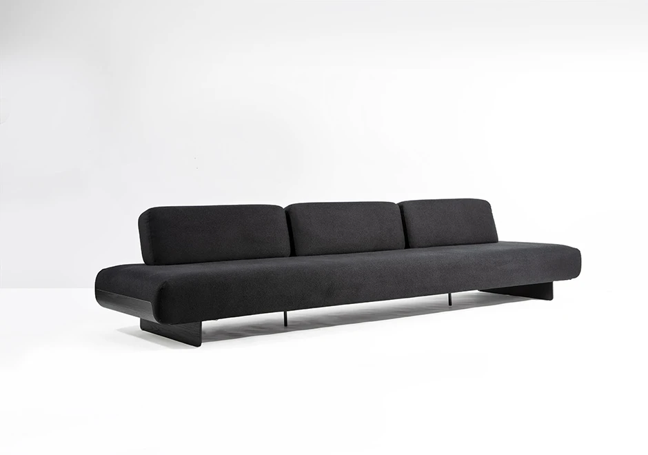 Sófa modular, com base de metal, revestido em espuma, estofado em tecido cinza, visto de lado em um fundo branco.