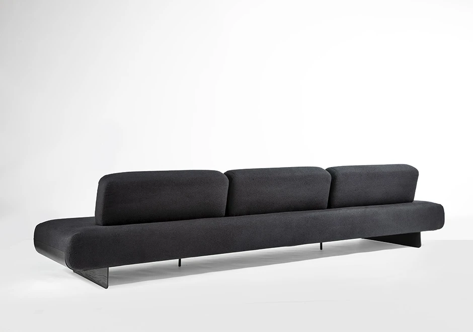 Sófa modular, com base de metal, revestido em espuma, estofado em tecido cinza, visto de costas em um fundo branco.