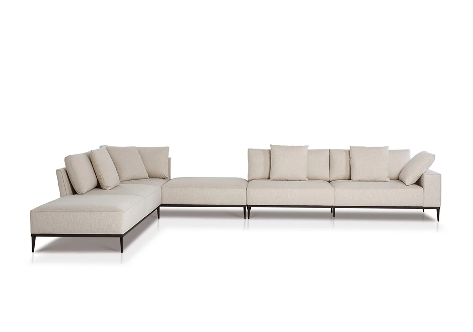 Sofá modular branco, com pés em aço escuro, com diversas almofadas, visto de frente, em um fundo branco
