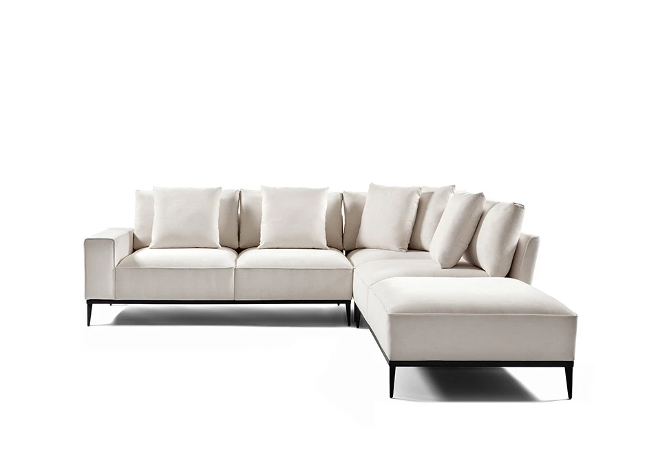 Sofá modular branco, com pés em aço escuro, com diversas almofadas, visto de frente, em formato de L, em um fundo branco
