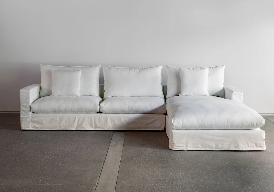 Sofá modular estofado em tecido branco e almofadas decorativas, visto de frente em um fundo branco.