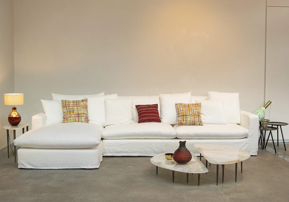 Sofá modular estofado em tecido branco e almofadas decorativas, visto de frente em uma sala de parede branca.