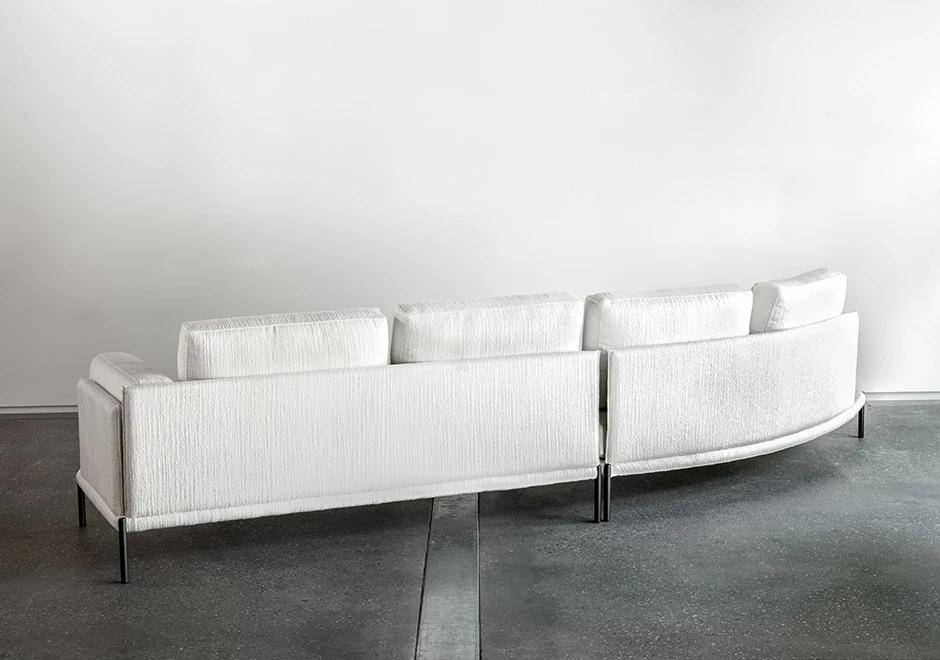 Sofá com escosto com pés de ferro, na cor branca, visto de costas com uma parede branca ao fundo.