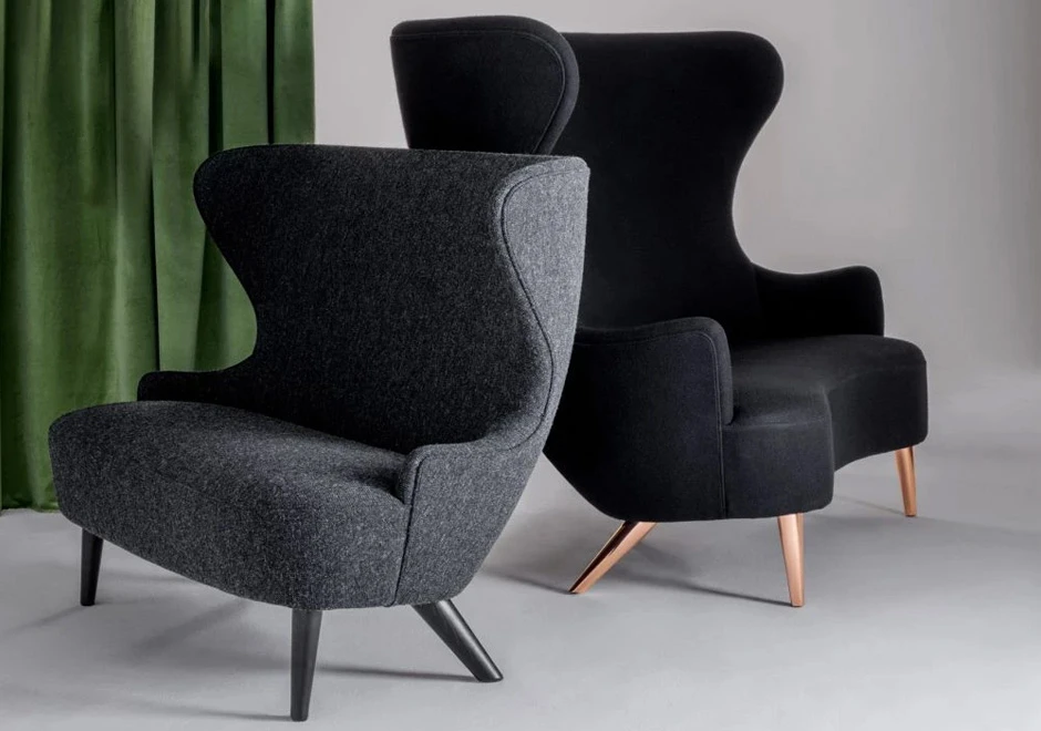 Sofá de design elegante, com estrutura de madeira, estofado em tecido cinza escuro, visto de lado em uma sala de parede branca.