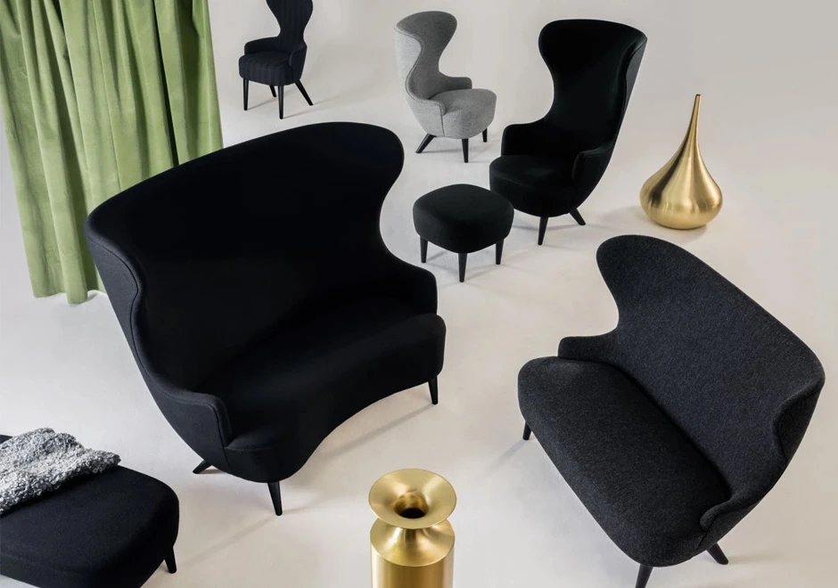 Dois sofás de design elegante, com estrutura de madeira, estofado em tecido preto, vistos de cima com um pufe em uma sala.