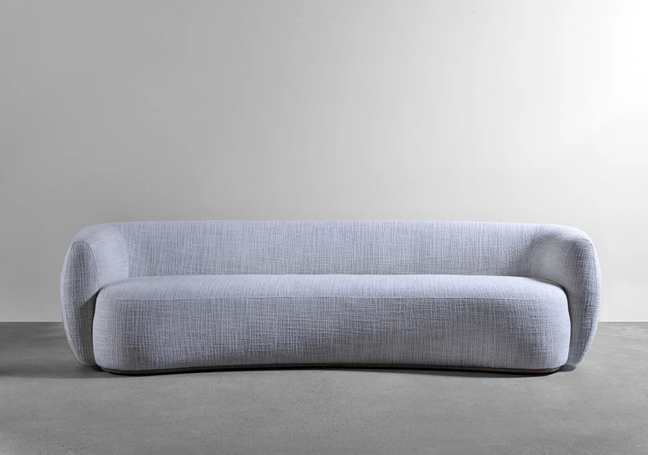 Sofá curvo, estofado em tecido cinza, visto de frente, em um fundo branco.