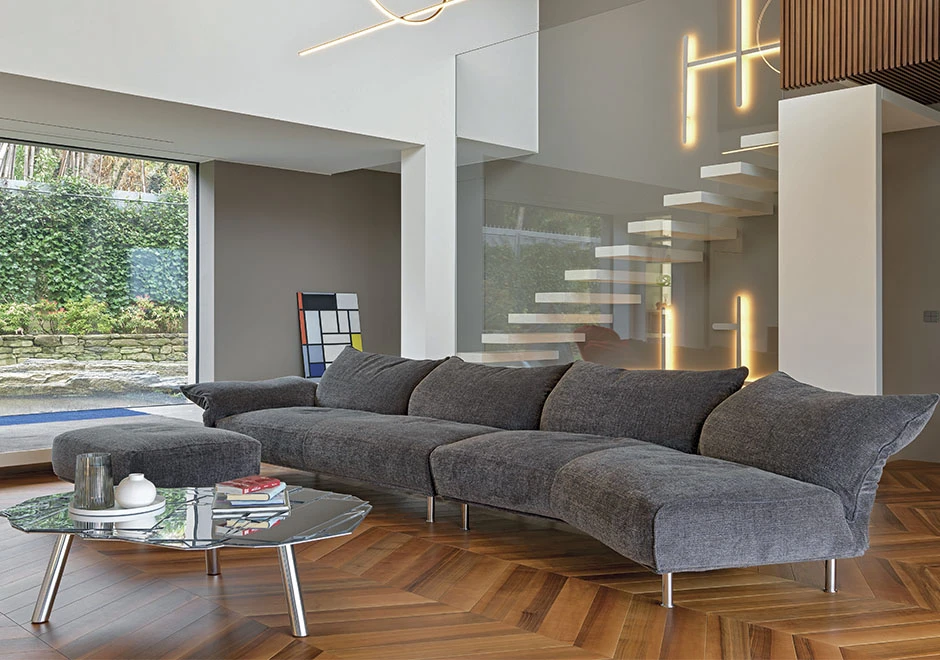 Sofá modular estofado em tecido cinza, visto de lado, em uma sala moderna.