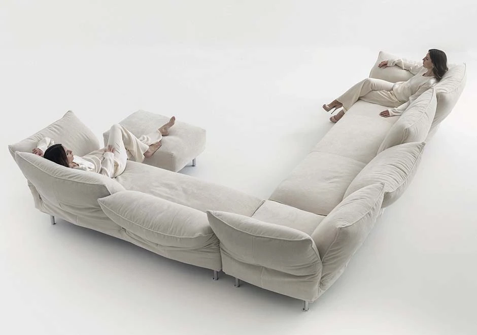 Sofá modular estofado em tecido branco, visto de costas, com duas pessoas sentadas, em um fundo branco.