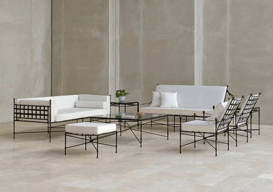 dois sofás contemporâneos, duas cadeiras e um banquinho com assentos e encostos brancos, almofadas brancas e estrutura fina e escura em um cenário cinza com duas mesas com tampos de vidro.