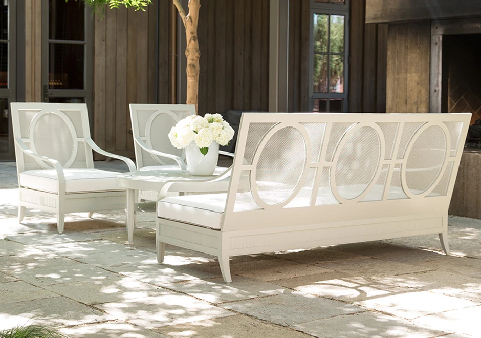 Sofá de área de lazer, com duas cadeiras, com estrutura, assento e encosto em alumínio branco, visto de costas, em uma area externa.