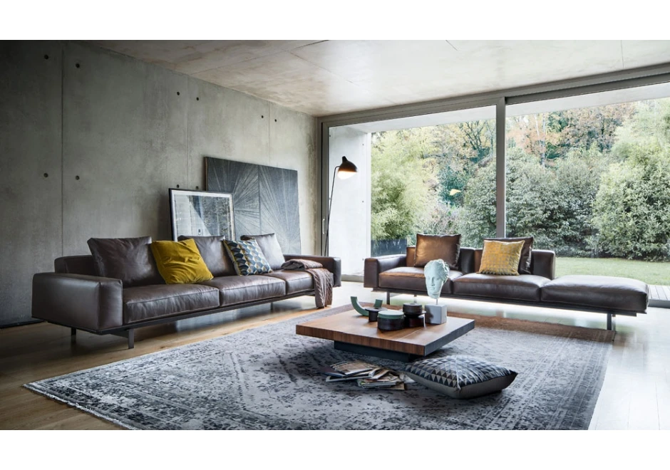 Sofá modular com estrutura de metal, estofado em couro marrom e almofadas decorativas, visto de frente em uma sala moderna.