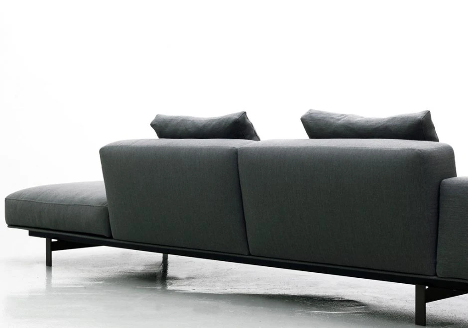 Sofá modular com estrutura de metal, estofado em tecido cinza e almofadas decorativas, visto de costas em um fundo branco.