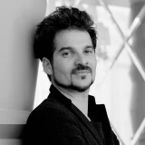 Foto de Jaime Hayon em preto e branco. Ele veste camisa escura e barba