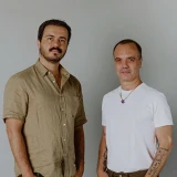 Pedro Ávila e André Bastos, lado a lado. Pedro veste camisa caqui e André, camiseta branca