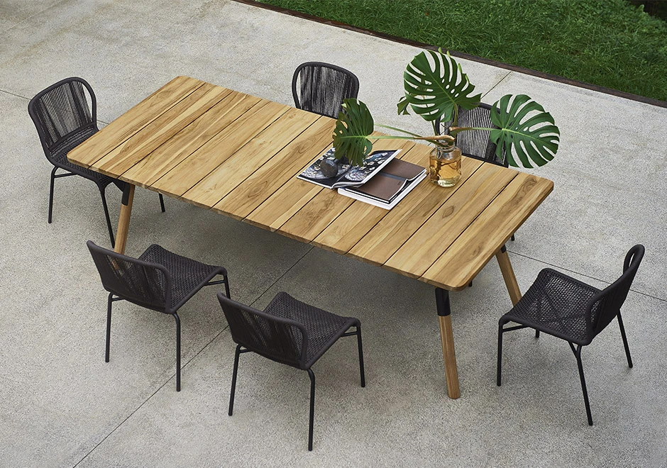 Seis cadeiras assinadas por Anki Gneib com estrutura de alumínio preto e assento preto revestido com fibra sintética trançada a mão, visto de vários angulos, em volta de uma mesa, em uma area externa.