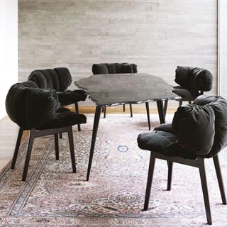 Cinco cadeiras Irmãos Campana com estrutura de madeira na cor preta, assento e encosto de veludo na cor preta em uma sala com parede de vidro e uma mesa espelhada.