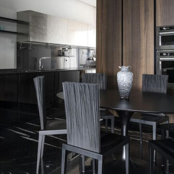 Detalhe de várias cadeiras Irmãos Campana com assento e pés em poliuretano moldado, encosto com 600 varetas flexíveis de PVC com placa de metal interna na cor preta, em volta de uma mesa, em uma sala de jantar.