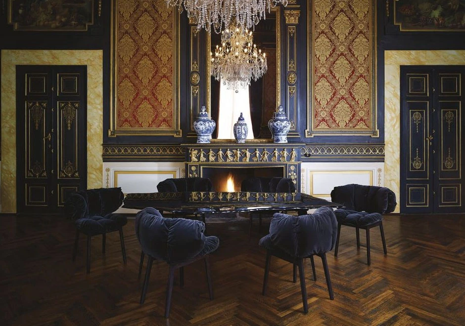 Cinco cadeiras Irmãos Campana com estrutura de madeira na cor preta, assento e encosto de veludo na cor azul em uma sala estilo clássico e uma mesa espelhada.