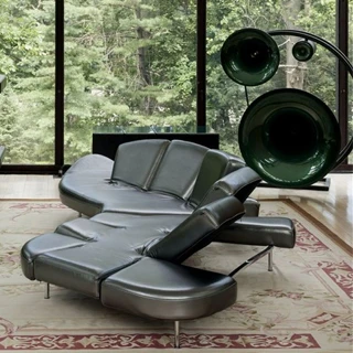 Sofá de design futurista, com estrutura de aço e mecanismo flexível com diferentes inclinações, na cor prata, visto de lado em uma sala moderna com parede de vidro.