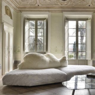 Sofá de design com estrutura de madeira, estofado em plumas e tecido na cor branco, visto de lado, em uma sala clássica.