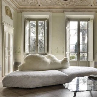 Sofá de design com estrutura de madeira, estofado em plumas e tecido na cor branco, visto de lado, em uma sala clássica.