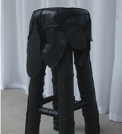 Banco de bar com estrutura de metal revestida em couro preto, visto de frente em um fundo branco.